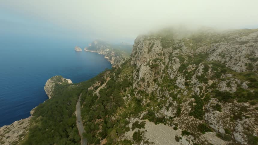 A rocky ridge high above the ocean with a winding road and fog