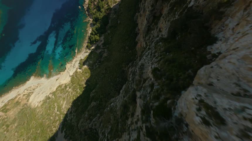 A steep mountain ridge near a clear blue lake stands tall under a cloudy sky