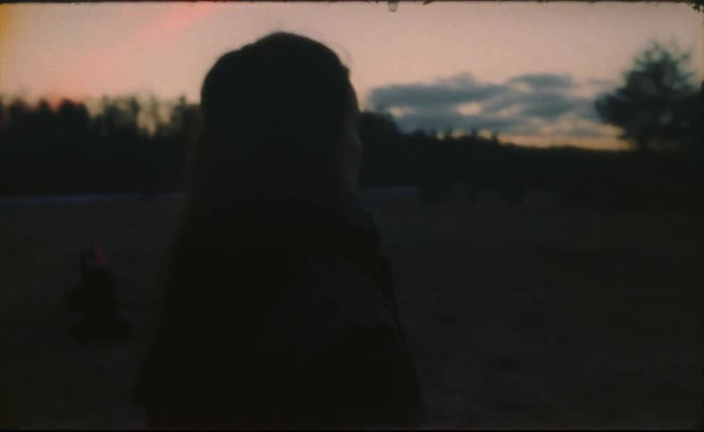 A woman is walking on a farm and there is a horse running in the field