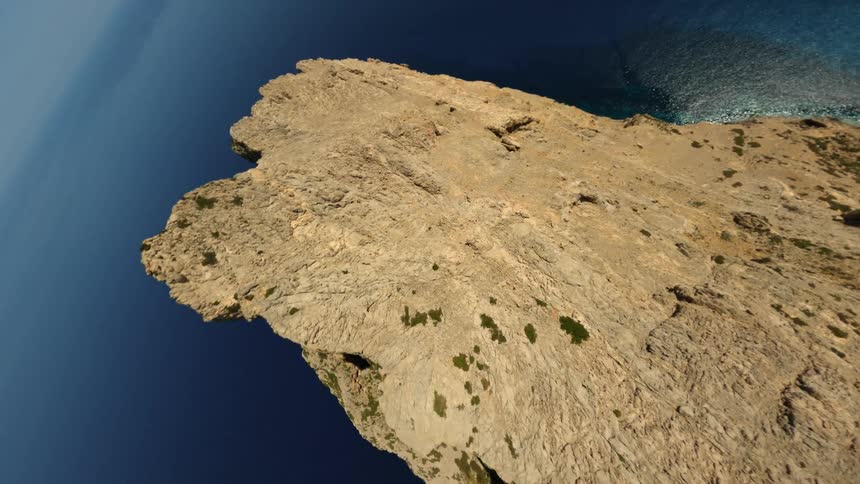 A steep mountain ridge near clear blue water stands tall along the shore