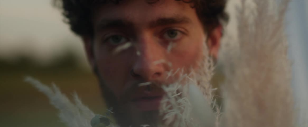 Close up of the face of a young man looking at the camera holding a bouquet of flowers