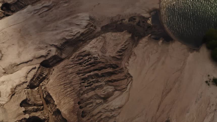 Top down twisting aerial view of the coast of jagged desert terrain close to a lake