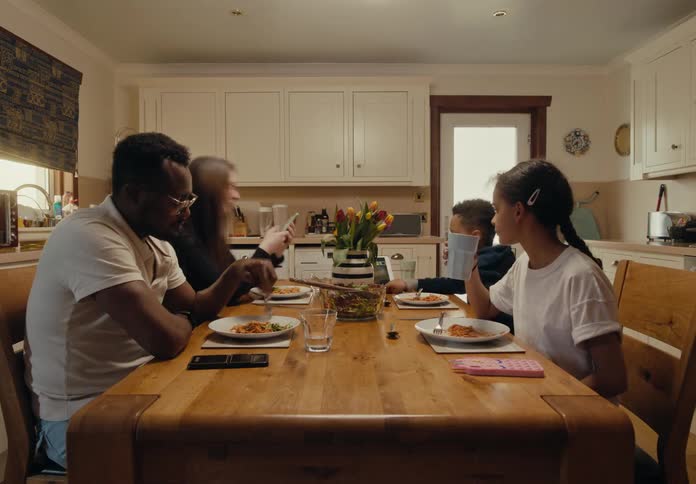 Timelapse of a family of four sitting at the kitchen table eating a meal together but each is using an electronic device