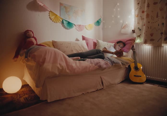A young girl relaxing on her bed next to a guitar and stuffed animal