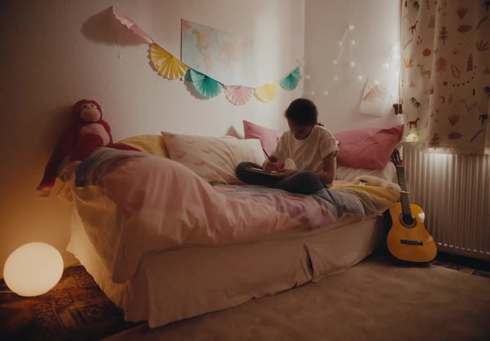 A girl sitting on her bed writing in a notebook picks up her phone to text