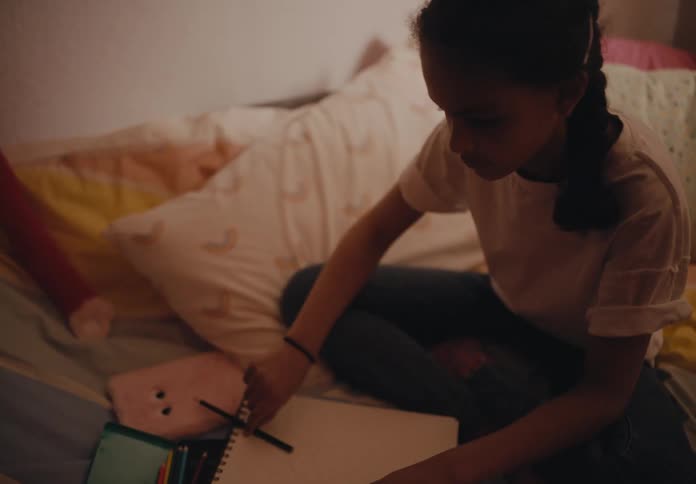 A girl is sitting on her bed using a phone and writing in a notebook