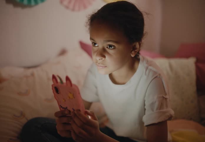 A girl is sitting on her bed intently playing with her phone  with the screen shining light on her face