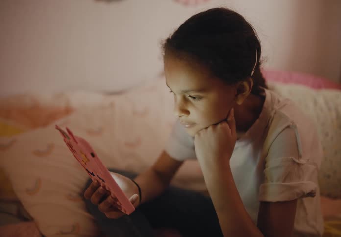 A girl is sitting on her bed playing with a smartphone that is shining light on her face