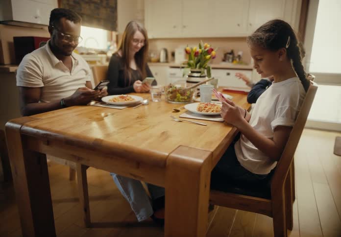 A family sitting at the dinner table together ignoring each other and playing on their phones