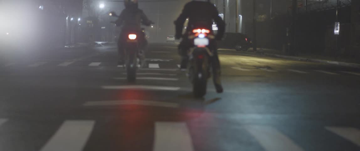 Two people are riding motorcycles at night