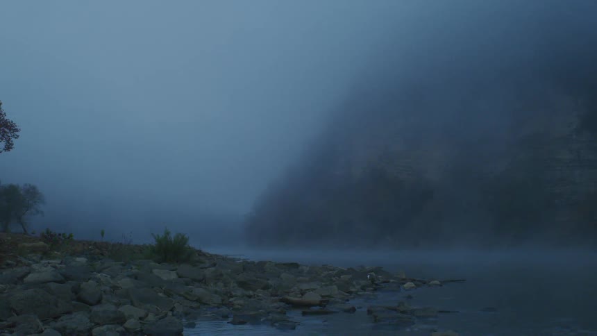 Fog hangs down all the way to the water of a river at the bottom of a mountain