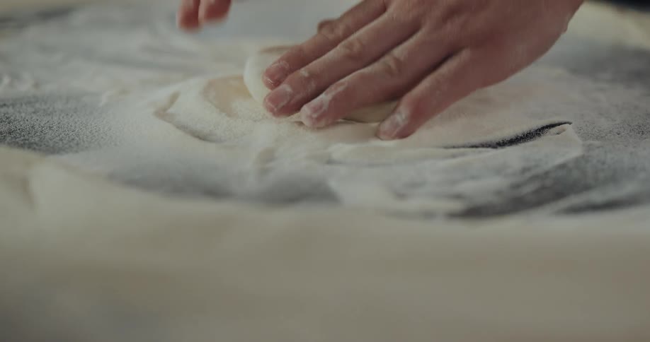 A person sprinkles flour on dough then starts working it