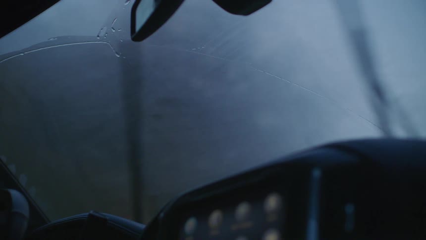 Windshield wipers wipe away drops of rain running down a windshield