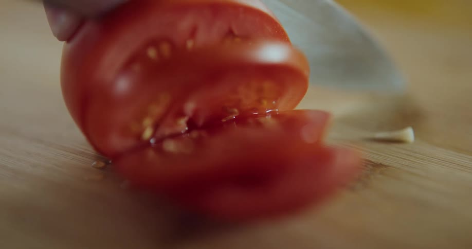 A person is slicing a tomato with a knife on a cutting board