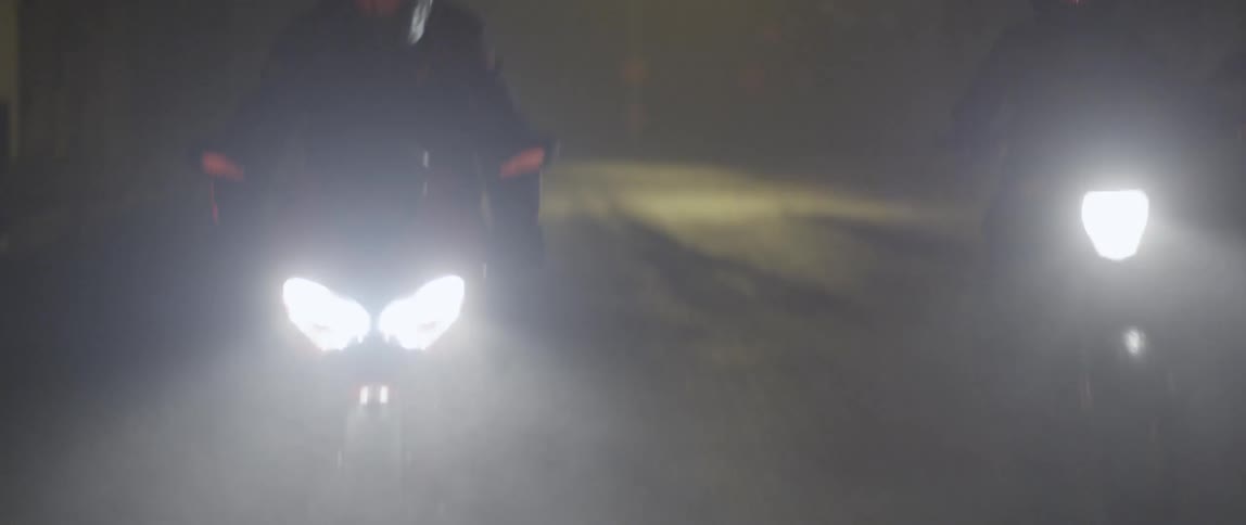 Motorcycle riders travelling along a foggy street at night