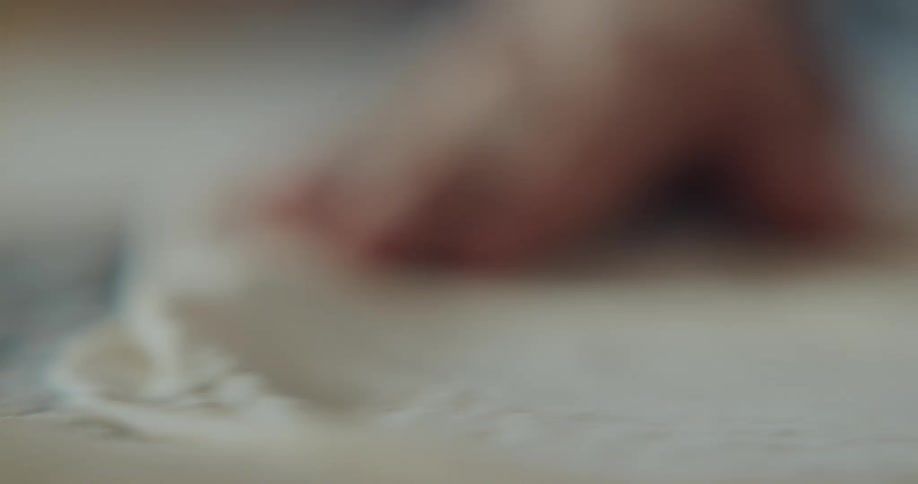 Person manipulates flat piece of dough on flour covered surface
