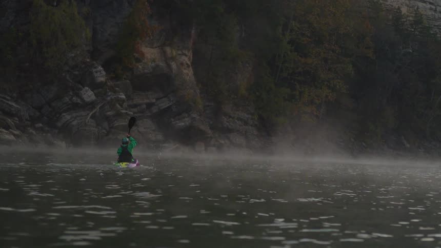 A man is kayaking on a misty river in a canyon