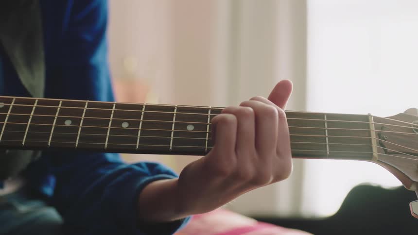 A person is playing the guitar sitting down inside there home