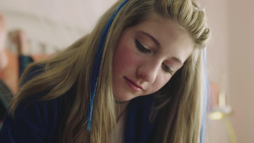 A teenager is sitting in her room and writing in a notebook