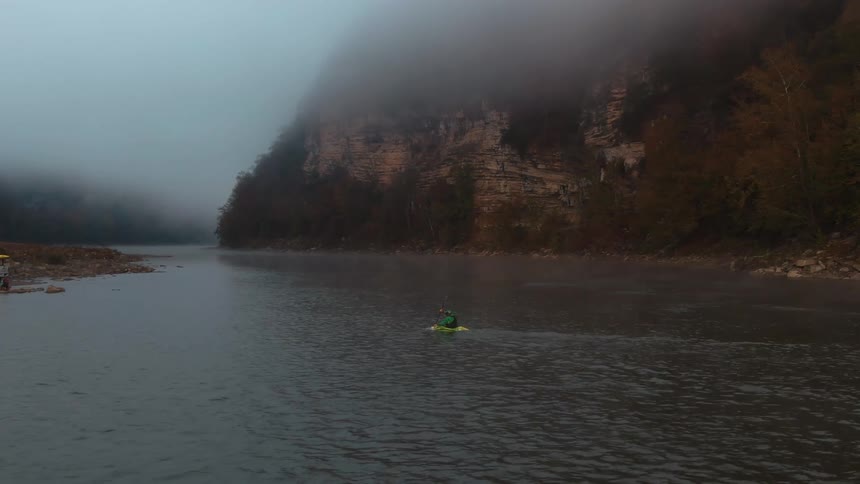 A man struggles as he rows a kayak toward shore against the rivers current