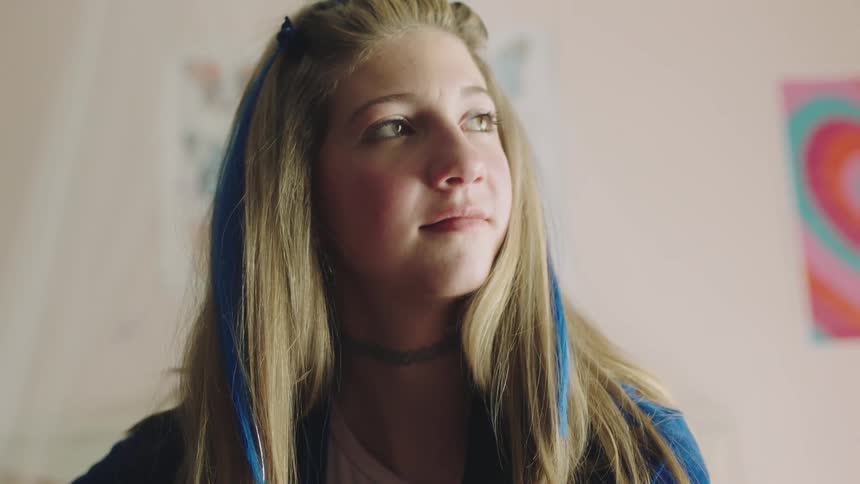 A teenage girl sitting in her bedroom playing the guitar smiling softly and closing her eyes
