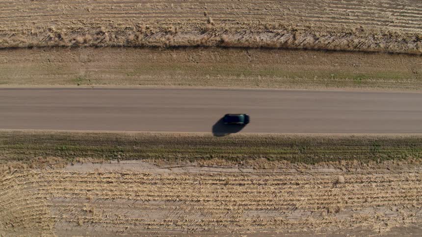 A vehicle travels along a road through a grassland during the day