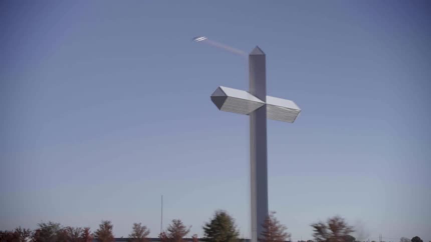 Large artistic metallic cross towers over nearby homes