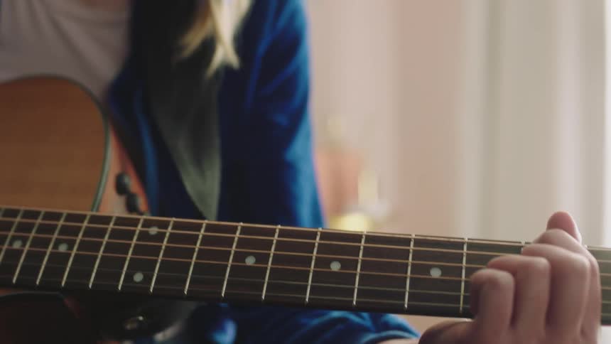Teenage guitarist holds guitar while sitting on bed