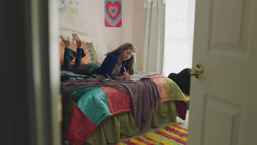 A teenage girl writing in a notebook while lying on her stomach in bed