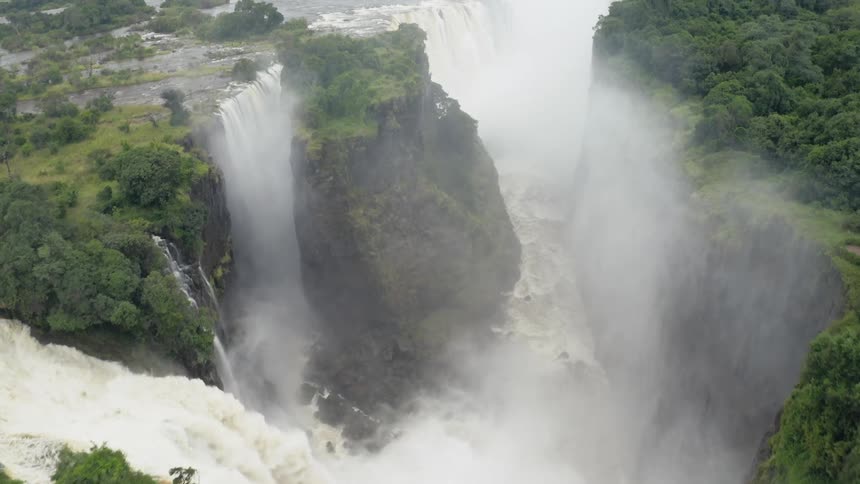 Aerial of misty clouds around massive jungle waterfall