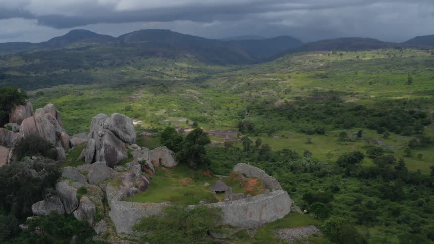 Ancient rock ruins overlooking a green valley with mountains in the distance
