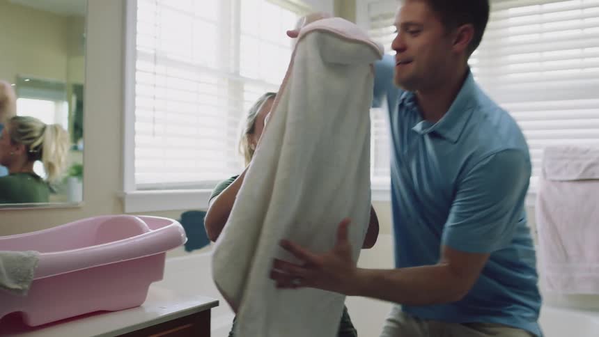 Young couple taking out a baby from a pink bathtub and wrapping him in a towel