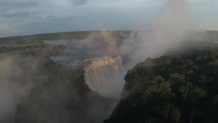 A river drops down over a cliff in a huge waterfall into a canyon and mist rises up over the landscape