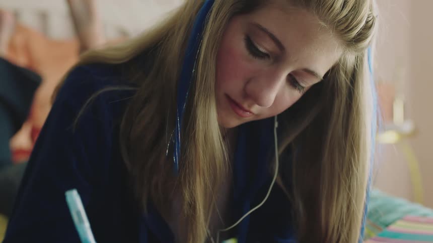 A teenage girl is writing in her notebook and sitting indoors