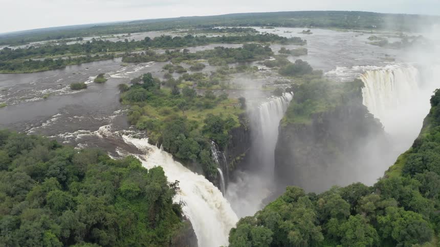 Several waterfalls flow down cliff as mist fills gorge in forest