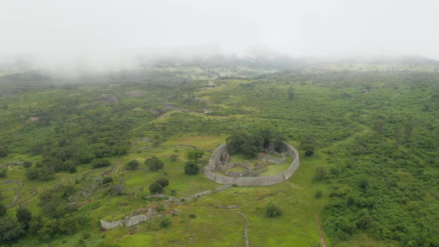Aerial view through misty clouds above stone walled ruins and forest