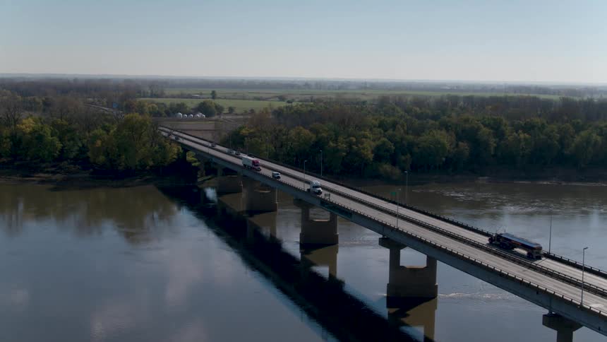 Cars and trucks traveling in both directions over a river on a bridge in a rural area
