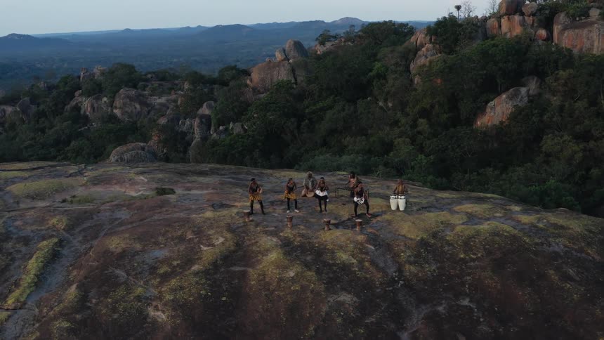People wearing traditional dress dance on small plateau near forest extending to the misty horizon