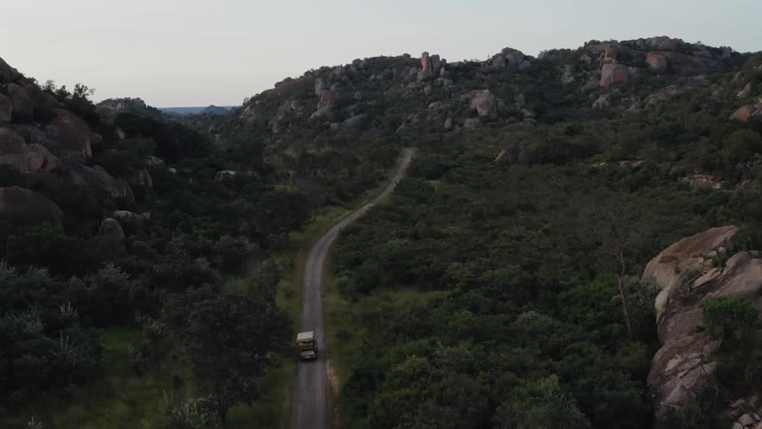 A tour bus is traveling on a road toward mountains with balancing rock formations