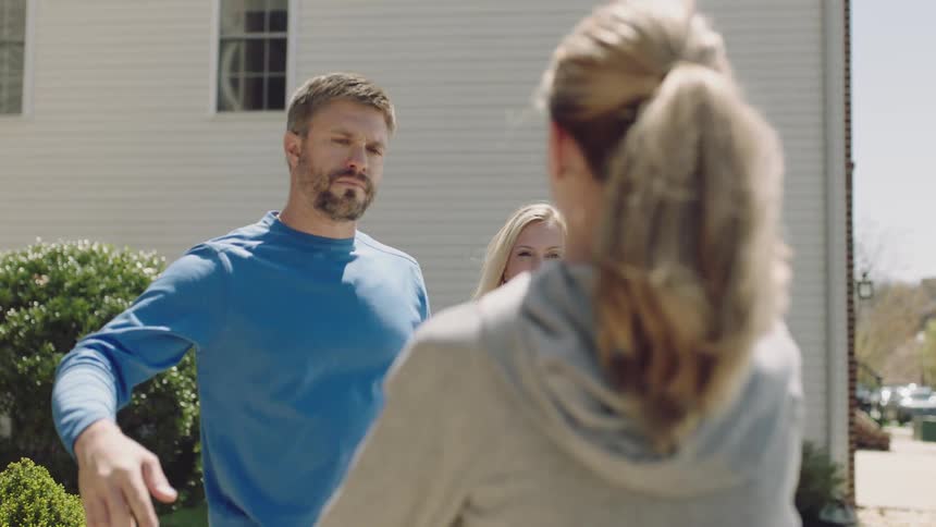 A mother and father hug their daughter as she packs her car in front of the house