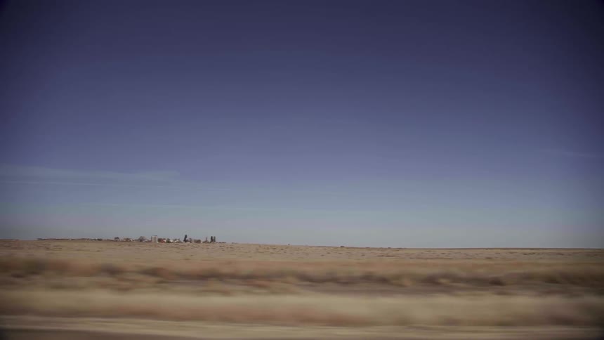 A long grass field leads to a town