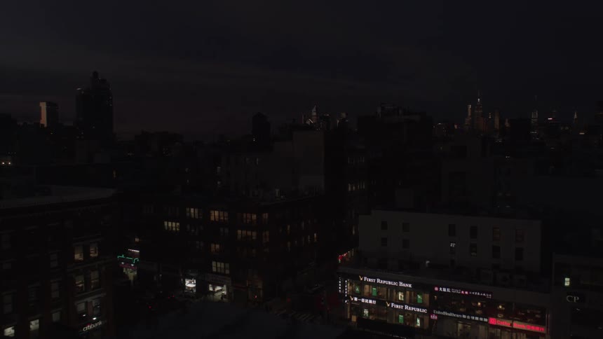 Traffic moves through intersection as sun sets and night falls with city skyline on the horizon