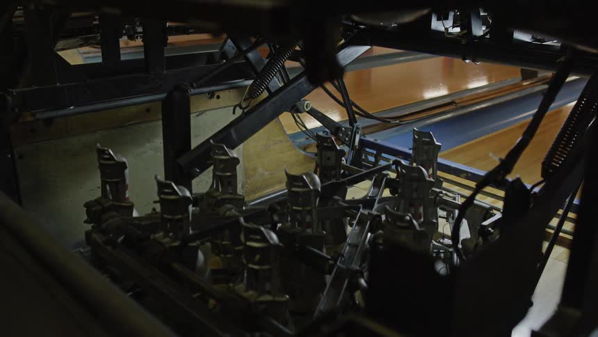 A machine in a bowling alley sets the ten pins up on at the end of the bowling lane