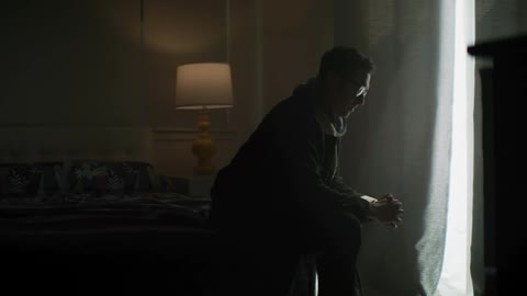A man is standing at a window with his hands together praying then he turns to look