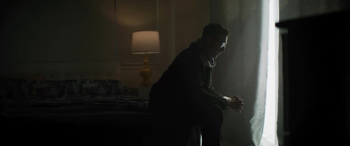 A man is standing at a window with his hands together praying then he turns to look
