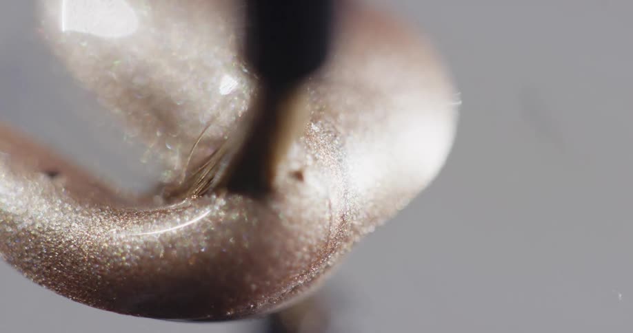 Tan metallic paint drops on to a surface and moves under the tip of a paint brush and it slowly moves as the paint sparkles