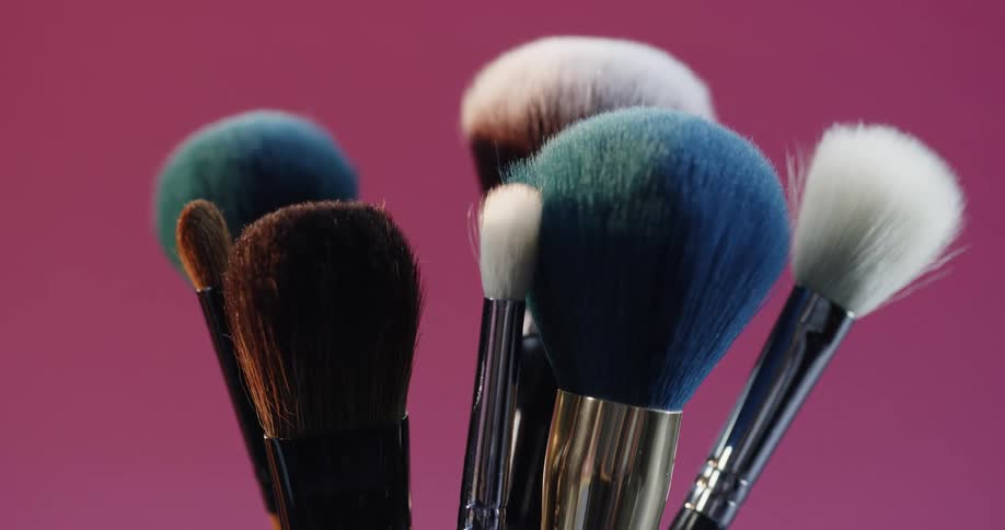 A collection of paint brushes are in a cup in a pink room