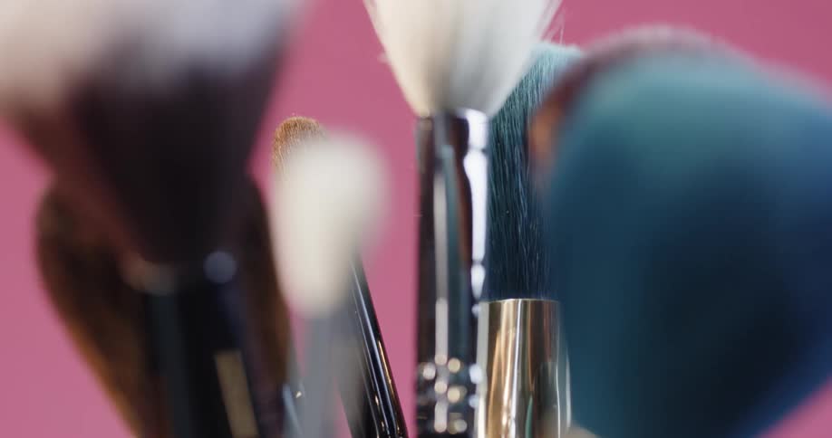 A collection of paint brushes are in a cup in a pink room