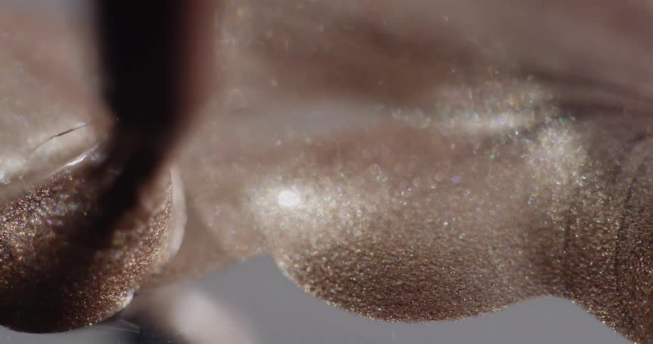 Tan metallic paint sparkles as a paint brush moves it across a surface
