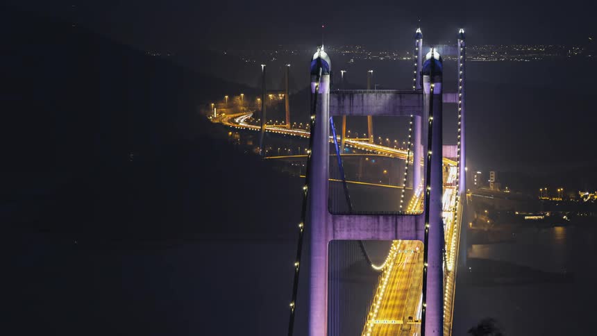 The sun sets and night falls on the tsing ma bridge in hong kong with traffic streaming across